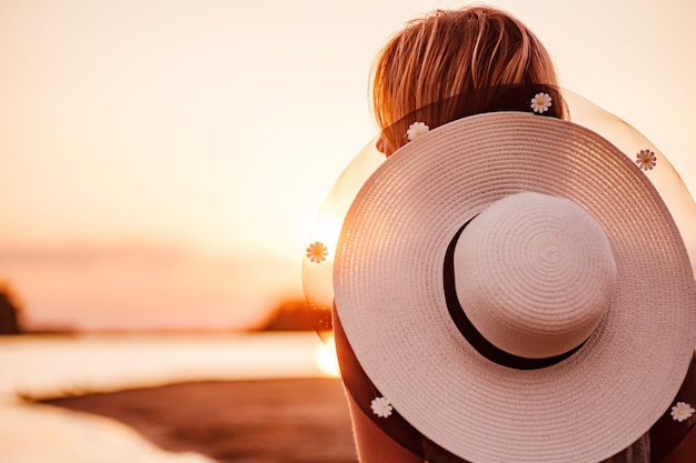 Une photo en gros plan d'une femme au coucher du soleil une belle jeune blonde avec un chapeau de paille blanc décoré de ...