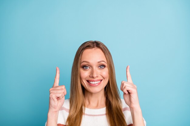 La photo en gros plan d'une femme positive joyeuse pointant vers le haut pour que vous puissiez vous abonner à son profil de médias sociaux isolé mur de couleur pastel bleu