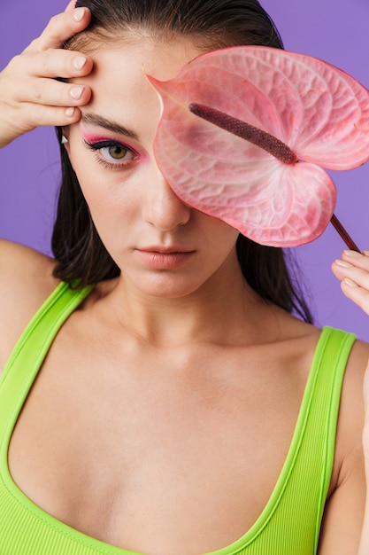 Photo en gros plan d'une femme séduisante caucasienne avec un maquillage lumineux tenant une fleur exotique