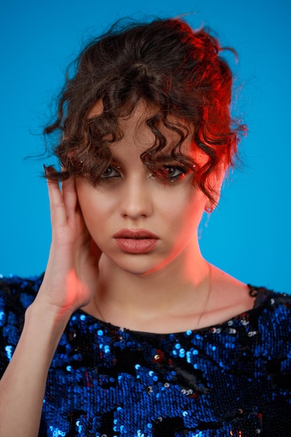 Photo en gros plan d'une fille aux cheveux bouclés posant ses mains sur son visage et debout sur un fond bleu Photo de haute qualité