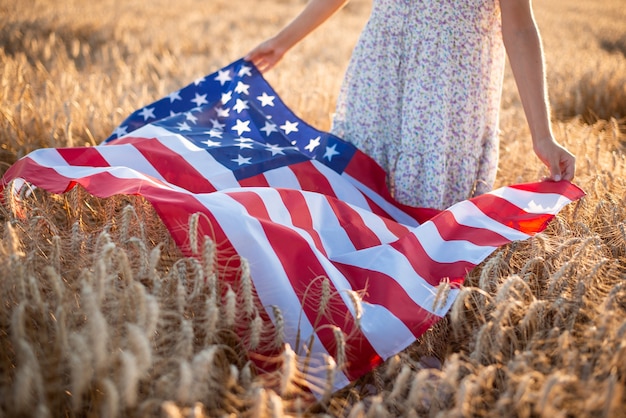Photo en gros plan d'une fille tenant le drapeau des États-Unis sur du seigle ou du blé mûrs. Jour de l'indépendance des États-Unis
