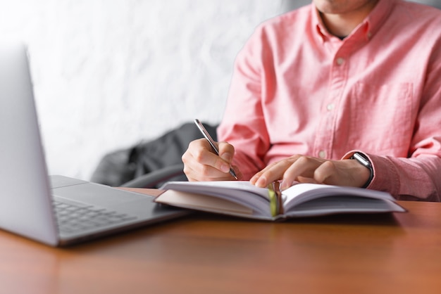 La photo en gros plan d'un homme assis dans le bureau et prendre des notes dans le planificateur