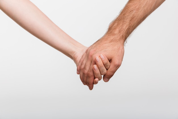 Photo gros plan d'un homme et d'une femme se tenant la main isolés sur un mur blanc.