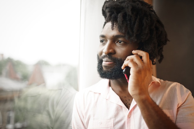 La photo en gros plan d'un homme noir d'âge moyen en chemise formelle parlant sur son téléphone près de la fenêtre