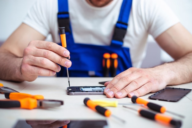Photo en gros plan d'un homme spécialisé pendant qu'il répare un smartphone cassé sur son lieu de travail avec des outils professionnels