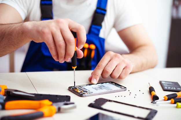 Photo photo en gros plan d'un homme spécialisé pendant qu'il répare un smartphone cassé sur son lieu de travail avec des outils professionnels