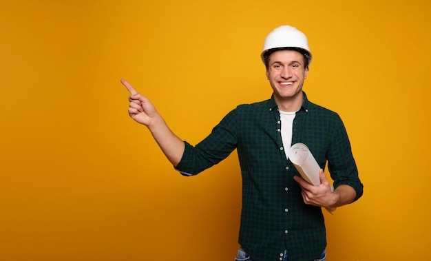 La photo en gros plan d'un jeune contremaître ou architecte heureux et confiant dans un casque de construction pose isolée sur fond jaune.