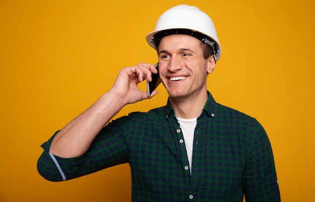 La photo en gros plan d'un jeune contremaître ou architecte heureux et confiant dans un casque de construction pose isolée sur fond jaune.