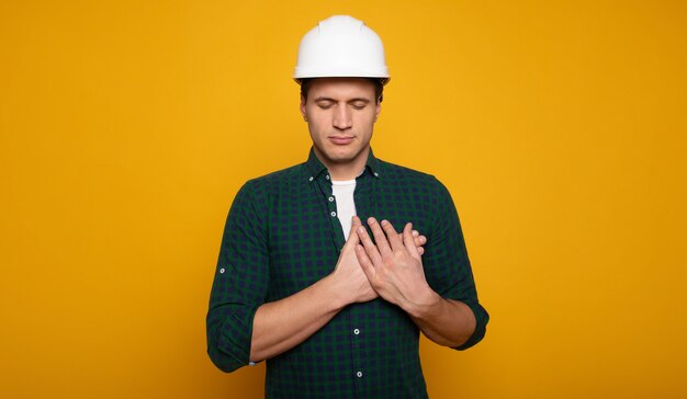 La photo en gros plan d'un jeune contremaître ou architecte heureux et confiant dans un casque de construction pose isolée sur fond jaune.