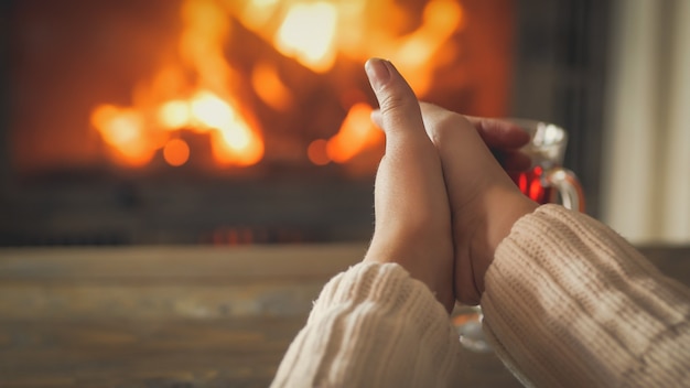 Photo gros plan d'une jeune femme se réchauffant les mains près de la cheminée en feu à la maison