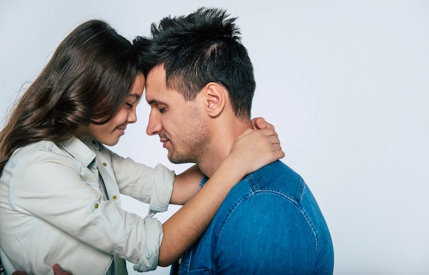 Photo en gros plan d'un jeune papa et de son petit enfant, qui s'embrassent tendrement et sourient, tout en regardant ensemble l'appareil photo.