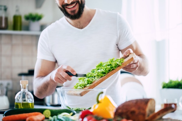 La photo en gros plan de jeunes mains mâles prépare une merveilleuse salade végétalienne fraîche dans la cuisine à la maison