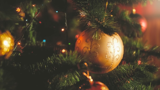 Photo en gros plan de lumières rougeoyantes et de boules colorées sur l'arbre de Noël à la maison. Arrière-plan parfait pour les vacances d'hiver et les célébrations