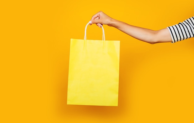 La photo en gros plan de la main féminine avec un sac à provisions coloré dans les mains isolé sur fond jaune