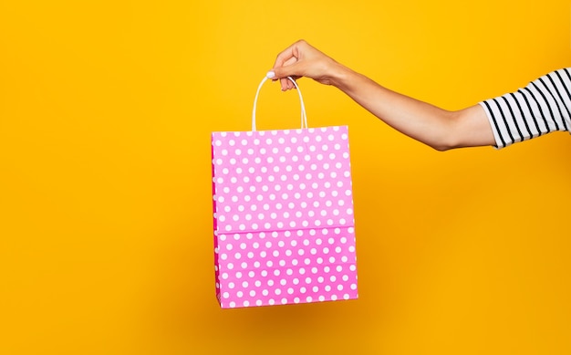 La photo en gros plan de la main féminine avec un sac à provisions coloré dans les mains isolé sur fond jaune