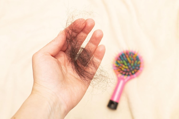 Photo en gros plan d'une main féminine tenant les cheveux perdus à la main sur un fond beige