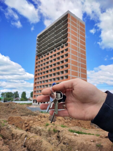 Photo En Gros Plan De La Main D'un Homme Tenant Les Clés D'une Nouvelle Maison Sur Fond D'un Immeuble Résidentiel Moderne