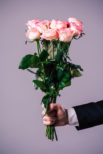 La photo en gros plan de la main masculine tient le bouquet de roses. Concepts de célébration, de vacances et de cadeaux. Date de la Saint-Valentin. Journée des amoureux