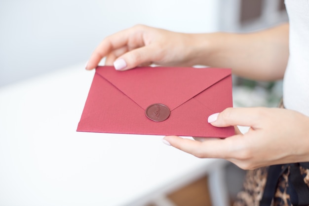 Photo gros plan de mains féminines tenant l'enveloppe d'invitation avec un sceau de cire, un certificat-cadeau, une carte postale, une carte d'invitation de mariage.