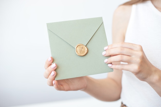 Photo en gros plan de mains féminines tenant une enveloppe d'invitation avec un sceau de cire, un chèque-cadeau, une carte postale, une carte d'invitation de mariage.