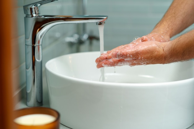 La photo en gros plan des mains des hommes se laver avec du savon au-dessus de l'évier