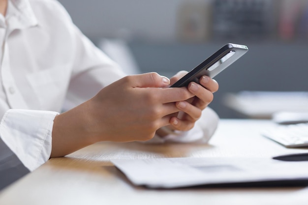 Photo gros plan les mains d'une jeune femme en chemise blanche tiennent un téléphone portable en tapant un