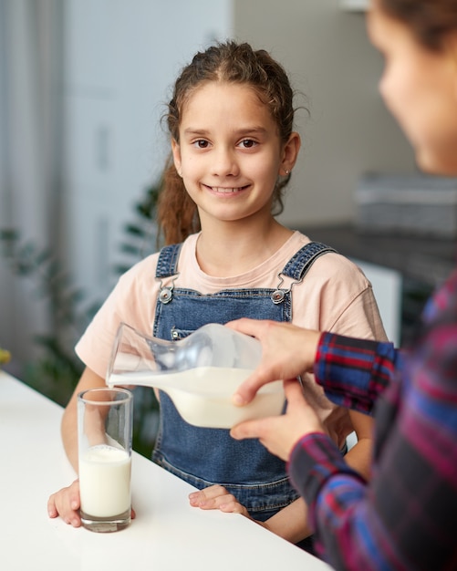 Photo gros plan d'une maman verse son lait de petite fille souriante mignonne pour le petit déjeuner, regardant la caméra.