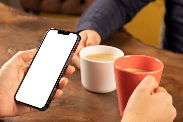 Photo en gros plan d'une maquette de smartphone à la recherche. Couple assis sur une table en bois au café.