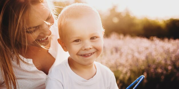 La photo en gros plan d'un petit garçon caucasien et sa mère posant dans un champ de lavande et sourire à la caméra