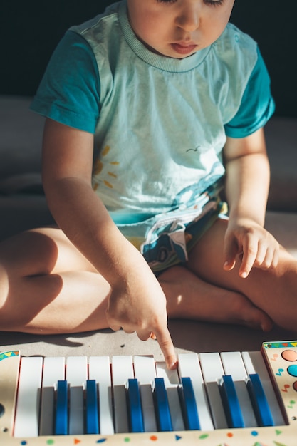 Photo la photo en gros plan d'un petit garçon jouant du piano jouet assis sur le sol concentré