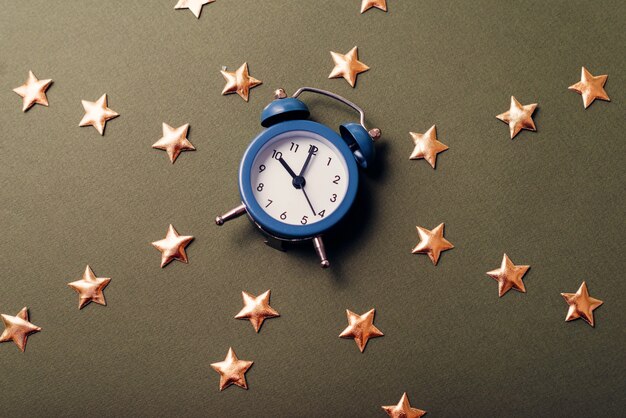 Une photo en gros plan d'une petite horloge bleue entre beaucoup d'étoiles sur une table sombre