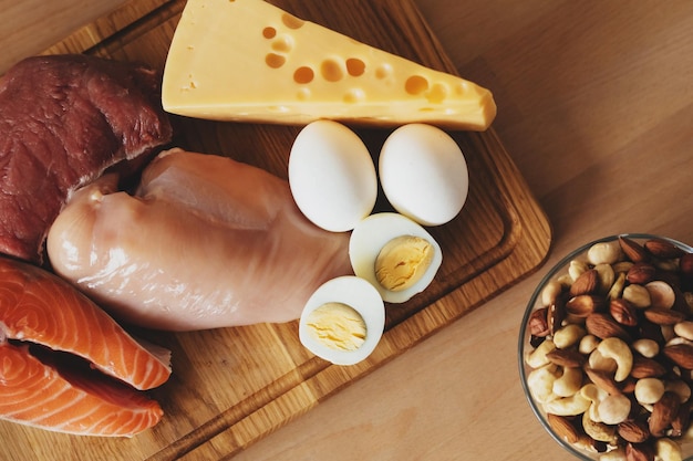 Photo en gros plan d'une planche de bois avec de la viande de poulet, du poisson, du fromage et des œufs à côté d'un bol avec des noix