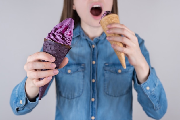 Photo en gros plan recadrée d'un adolescent heureux et délicieux mangeur de nourriture fou positif tenant de la crème glacée dans les mains essayant de manger à la fois un fond gris isolé portant un jean chemise décontractée en jean