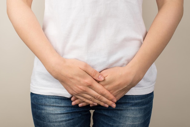 Photo en gros plan recadrée d'une jeune femme en t-shirt blanc et jeans tenant ses mains sur l'entrejambe sur fond gris isolé