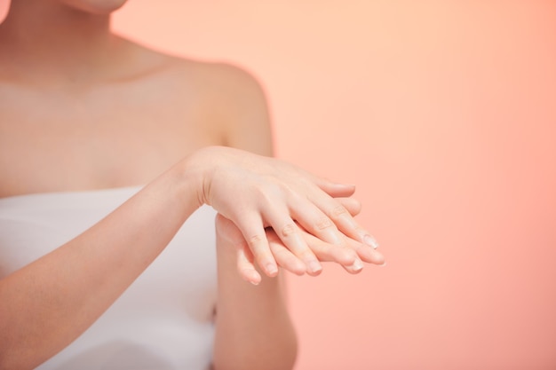 Photo en gros plan recadrée des mains d'une jeune femme appliquant de l'huile corporelle crème hydratante pour un effet lisse au spa