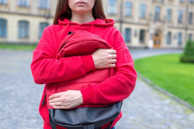 Photo en gros plan recadrée de sérieux sans sourire sur le visage d'un jeune étreignant son sac debout près de l'entrée du bâtiment