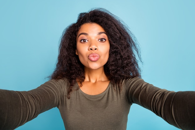 La photo en gros plan de rêve romantique sensation romance peau noire fille en vacances prendre selfie appel vidéo envoyer des baisers aériens porter chemise élégante isolée sur mur de couleur bleue