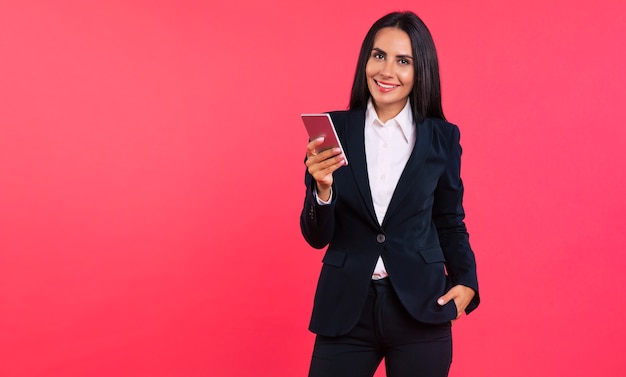 Photo en gros plan d'une superbe jeune femme d'affaires brune vêtue d'une tenue élégante, qui tient un smartphone dans les mains et sourit tout en vérifiant le flux