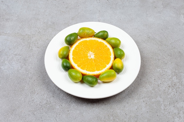 La photo en gros plan de tas de kumquats avec une tranche d'orange sur une plaque blanche.