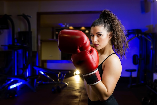 La photo en gros Portrait de jeune belle femme sportive en gants de boxe rouges dans la salle de gym