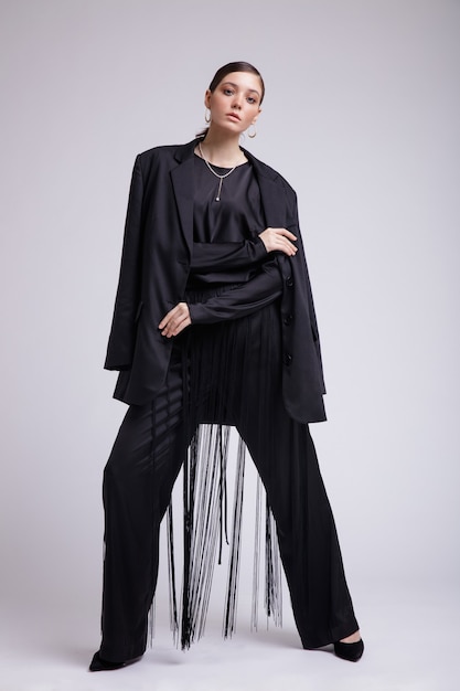 Photo haute couture de femme en veste noire chemisier pantalon à franges accessoires sur fond gris