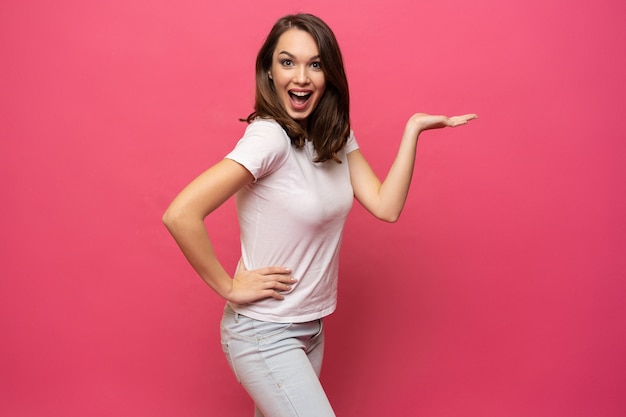 Photo de l'heureuse jeune femme debout isolée sur fond rose. À la caméra montrant le pointage de copyspace.