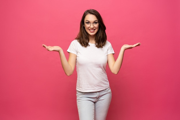 Photo de l'heureuse jeune femme debout isolée sur fond rose. À la caméra montrant le pointage de copyspace.