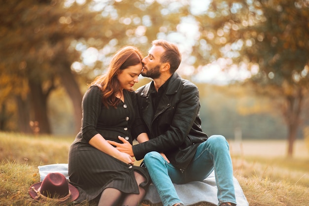 Photo de l'heureux couple enceinte assis sur le banch dans le parc, beau baiser de front