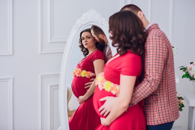 Photo de l'heureux futur père regarde sa femme enceinte. mari et enceinte sur un fond de miroir.