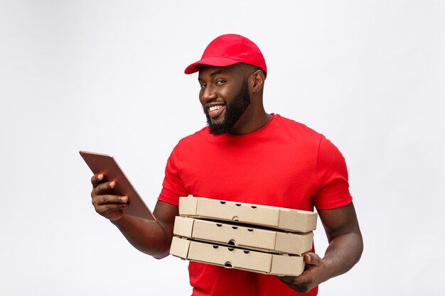 Photo de l'heureux homme afro-américain du service de livraison en t-shirt rouge et casquette donnant la commande de nourriture et tenant des boîtes à pizza