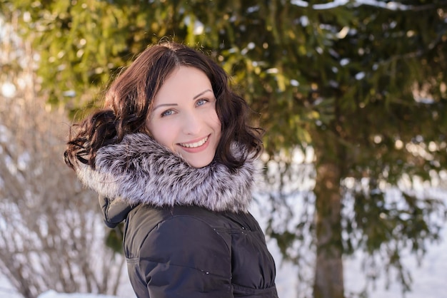 Photo d'hiver avec une jeune fille adulte dans le parc dans la neige près de l'arbre en journée ensoleillée