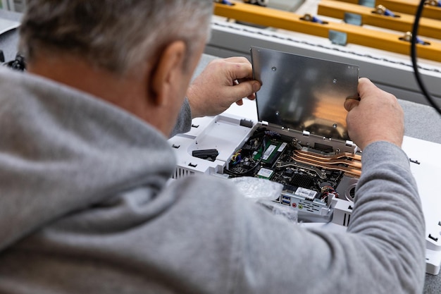 Photo d'un homme adulte portant un chandail gris qui assemble un bloc système de moniteur d'ordinateur sur un convoyeur