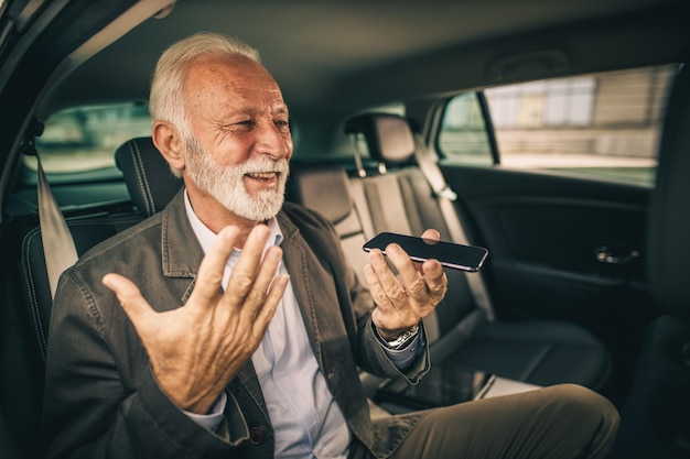 Photo d'un homme âgé qui a réussi à utiliser un smartphone alors qu'il était assis à l'arrière d'une voiture pendant son trajet d'affaires.