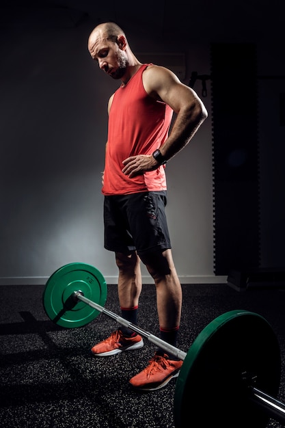 Photo d'un homme athlétique bodybuilder musclé se préparant à s'entraîner avec des haltères sur un studio sombre.